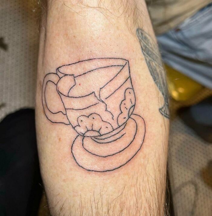 Line-drawn tattoo of a c*****d tea cup and saucer on a person’s arm, illustrating a wild tattoo fail forever problem.