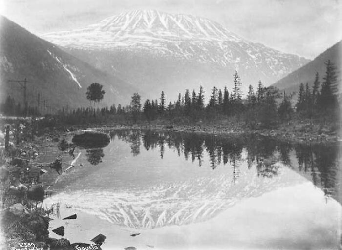 Black and white rare photograph showing a mountain reflected in a lake, showcasing history restored from glass negatives.
