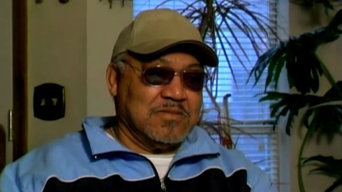 Man in sunglasses and cap sitting indoors, sharing an unfortunate story about winning a large lottery prize.