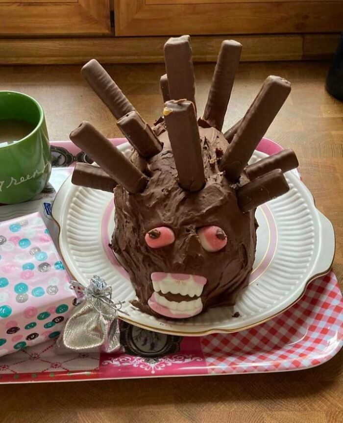 Chocolate cake with cylindrical decorations and googly eyes, resembling a hedgehog on a plate.