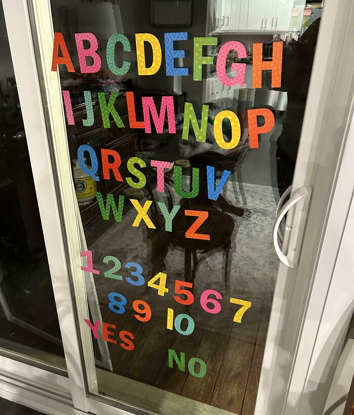 Colorful alphabet and numbers stuck on a glass door, reflecting an indoor scene.