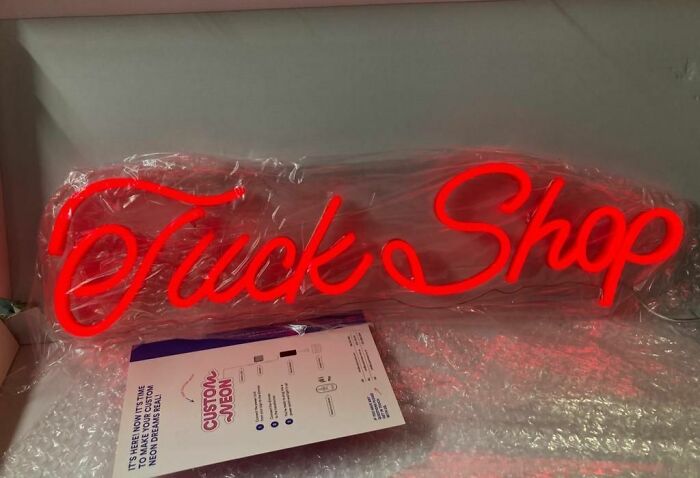 Neon sign typo error displaying "Tuck Shop" in red letters, suggesting someone's bad day.