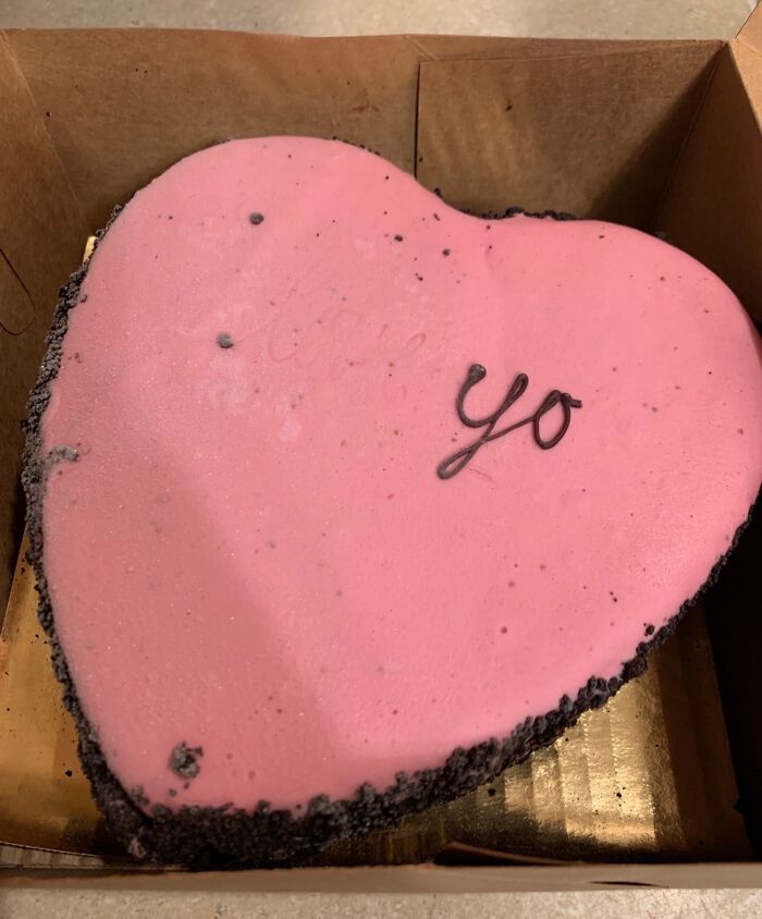 Heart-shaped pink cake with the word "yo" written on top, resembling a baking mishap.