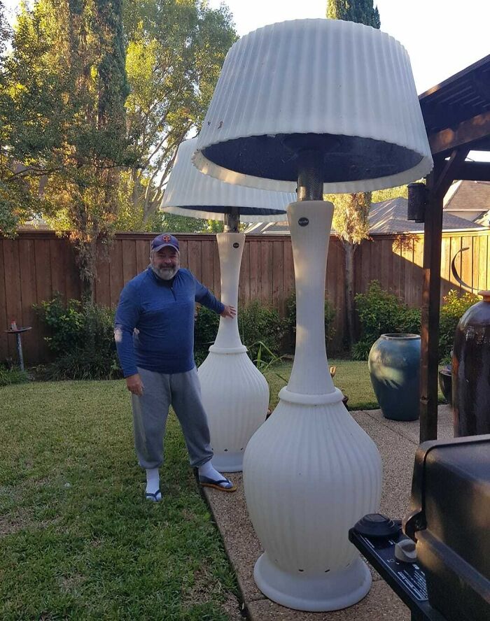 A man in a backyard poses beside oversized white lamp decor, possibly having a worse day.