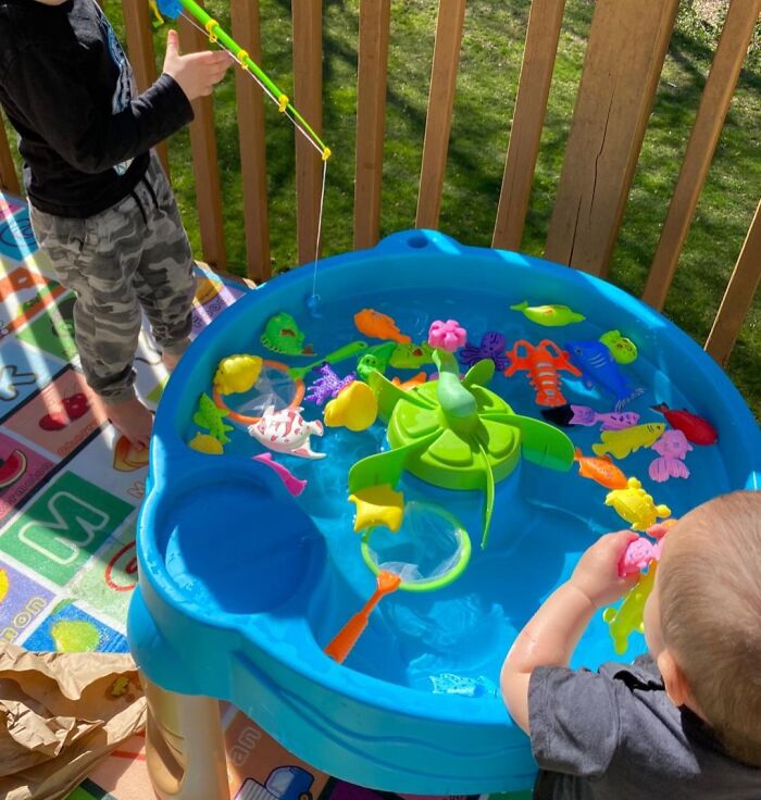 Kids playing with colorful water toys in a blue fishing game table on a sunny outdoor deck, popular kids toys revealed by teachers.