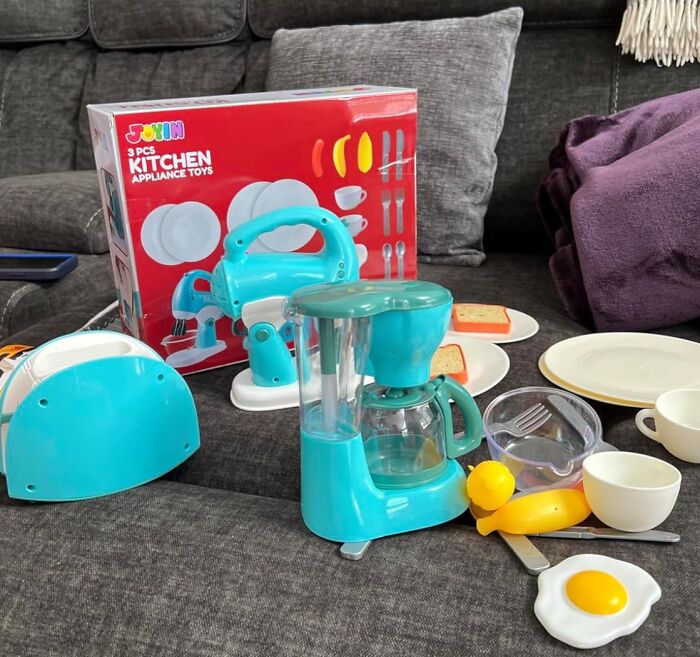 Children's toy kitchen appliances including a toy blender, coffee maker, and pretend breakfast set on a couch.