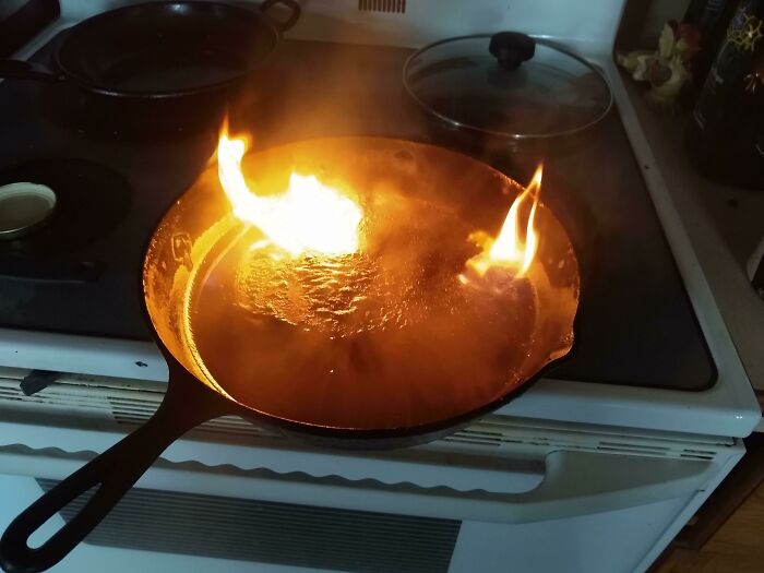Cast iron skillet on stove with flames, highlighting mistakes by first responders when dealing with kitchen fires.