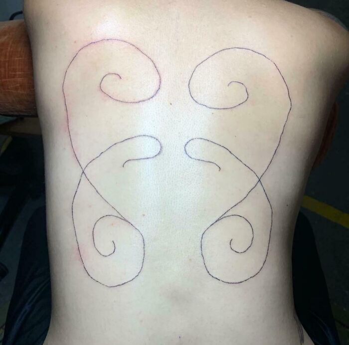 Minimalist black line tattoo on a person’s back showing an abstract design, a wild tattoo fail example.