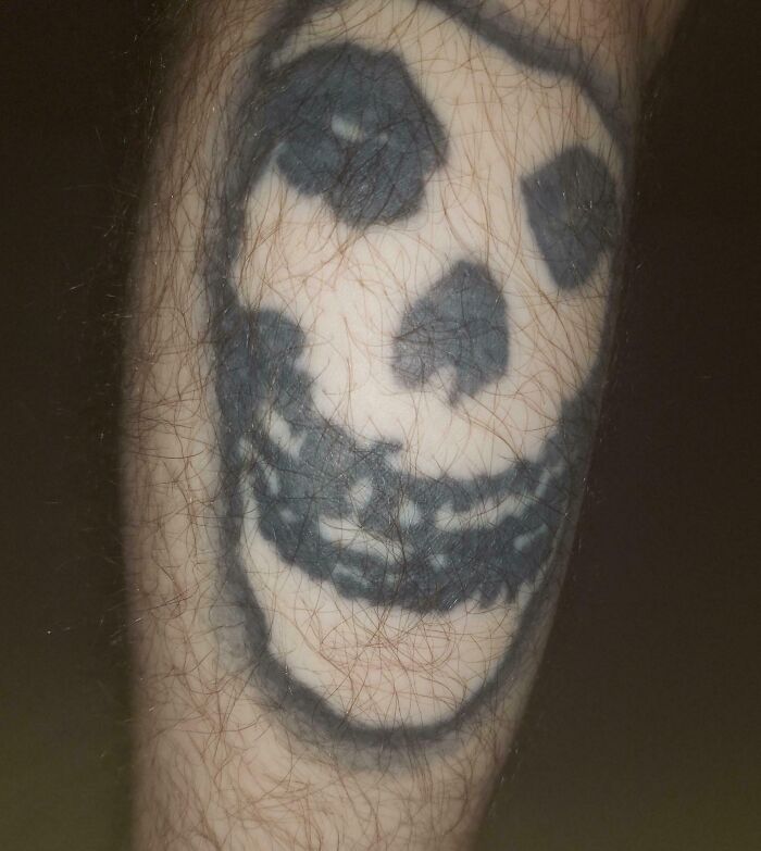 Blurry skull tattoo on hairy arm showing one of the wild tattoo fails that became a permanent problem.