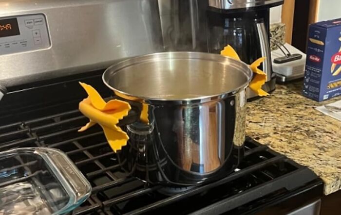 Steaming pot on stove with handles shaped like bowtie pasta, showcasing creative food-shaped objects.