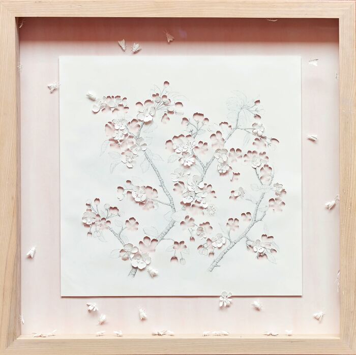 Intricate mini world paper art by Peter Callesen, featuring delicate cut-out floral patterns, framed in light wood.