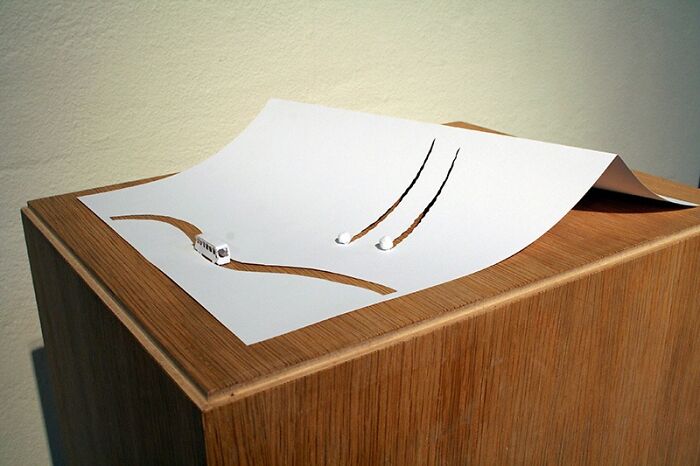 Miniature paper world by Peter Callesen, featuring cutouts and a tiny bus on a wooden surface.