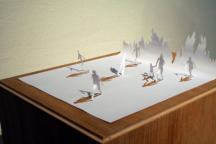 Miniature paper worlds by Peter Callesen featuring cut-out figures on a wooden surface.