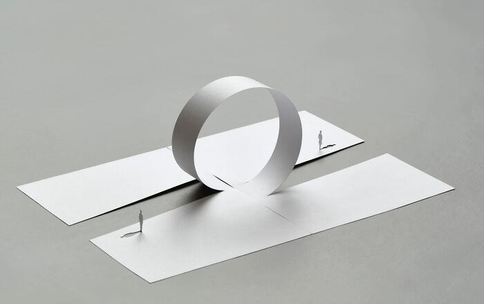 Mini worlds made from paper by Peter Callesen depicting tiny figures and a loop structure on a flat surface.