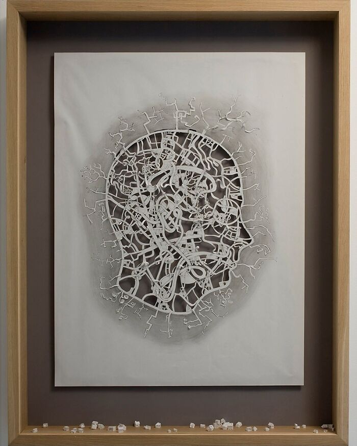Intricate paper art shaped like a human head, showcasing detailed, abstract patterns in a wooden frame.