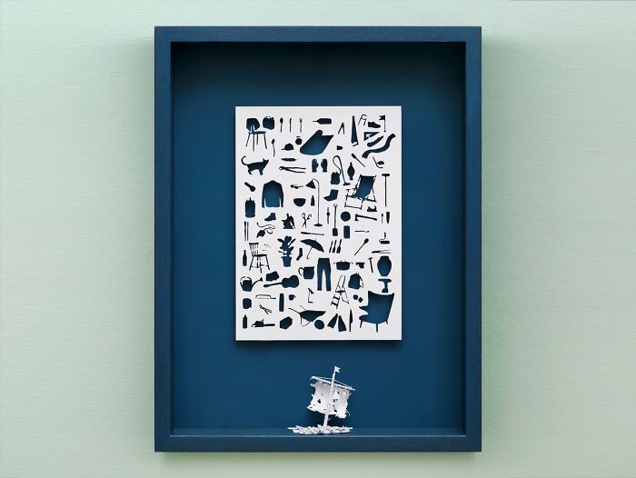 Paper art depicting a mini world in a blue frame, featuring intricate cutouts and a small ship below.