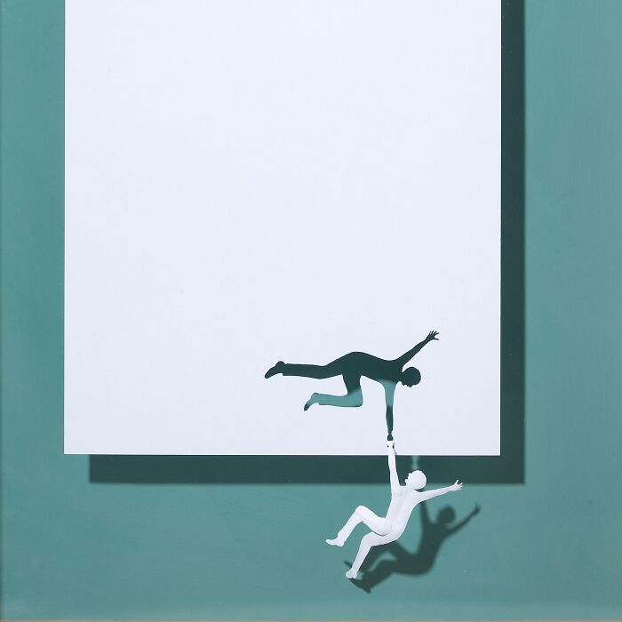 Paper art by Peter Callesen depicting two silhouettes interacting with a large white sheet, creating a mini world illusion.