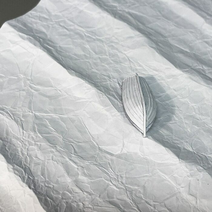 Miniature paper boat crafted by Peter Callesen on textured paper, showcasing intricate detail.