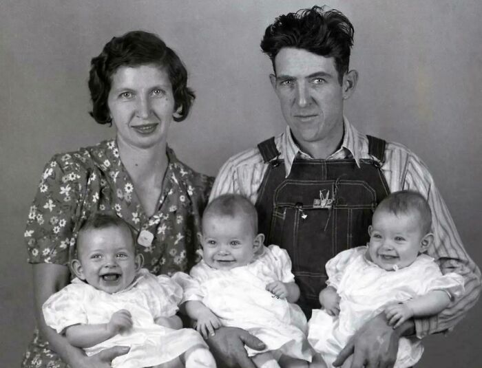 Vintage family portrait with a couple holding three smiling babies, showcasing life in the past.