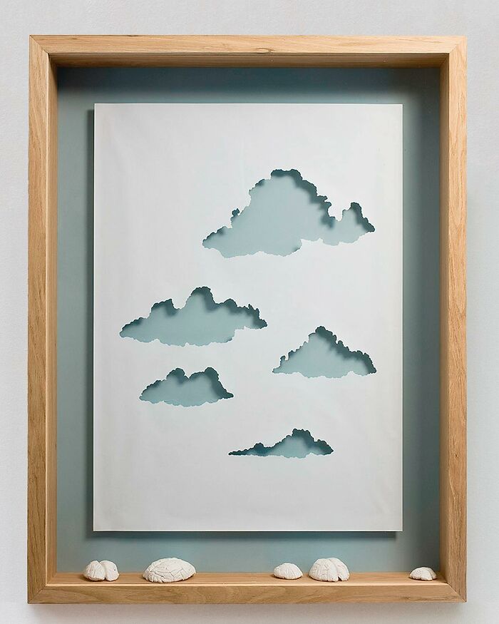 Paper art of clouds in a wooden frame, showcasing intricate cut-out details.