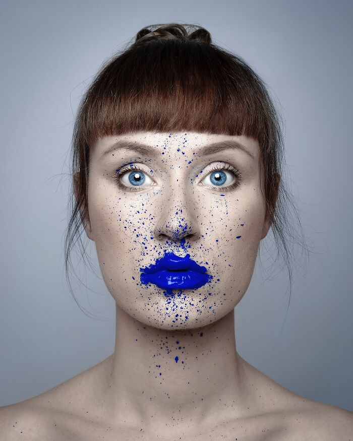 Artist's surreal self-portrait with blue paint splatters on face and lips, showcasing creative Photoshop technique.