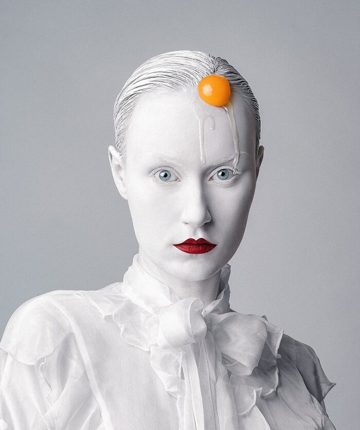 Surreal self-portrait with a woman in white makeup and red lipstick, featuring an egg yolk on her head, created with Photoshop.