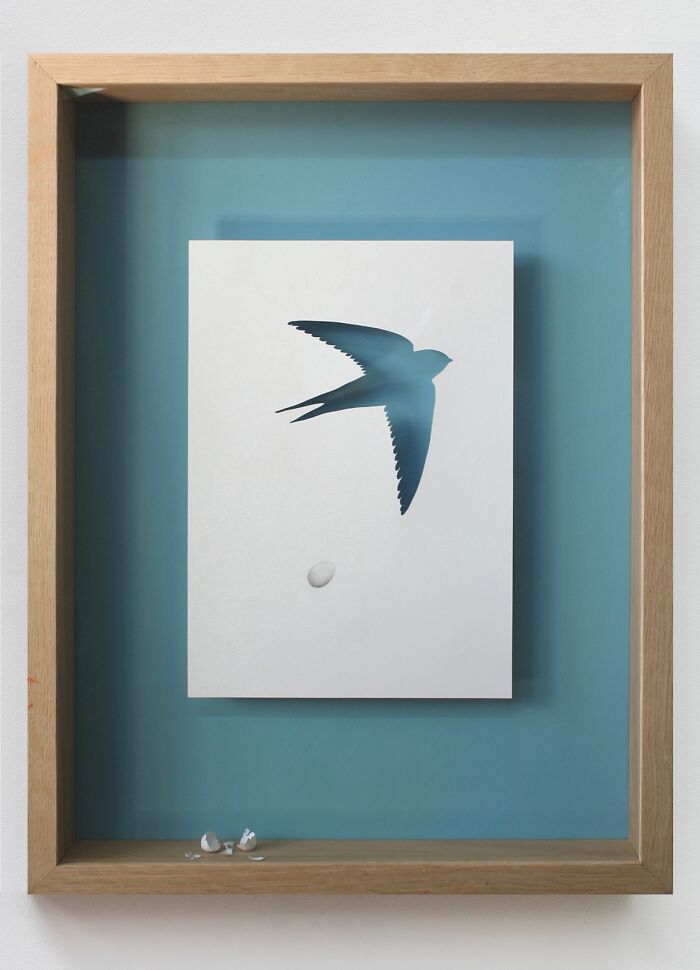 Paper art by Peter Callesen featuring a bird cut-out in white paper against a blue background.