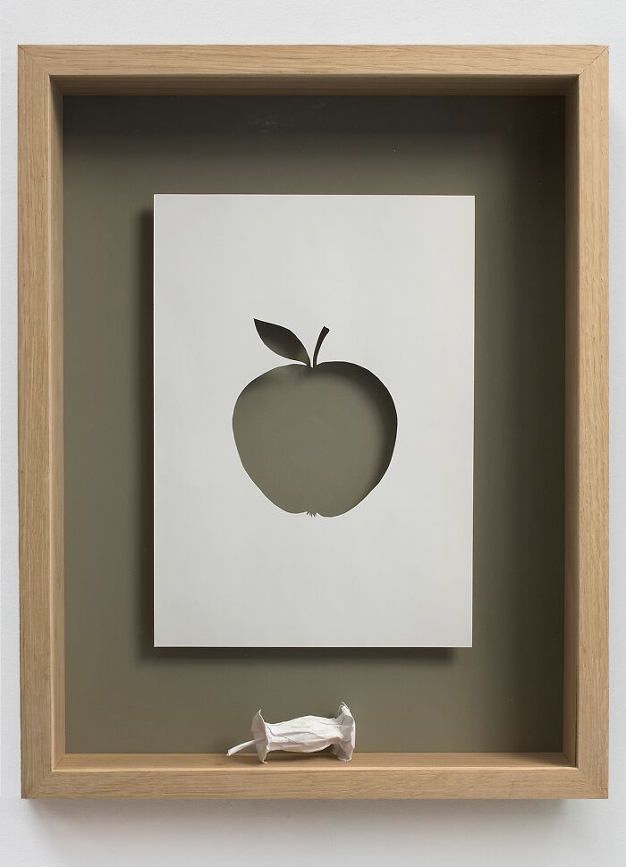 Paper art by Peter Callesen featuring an apple cutout in a framed sheet with a small three-dimensional paper apple.