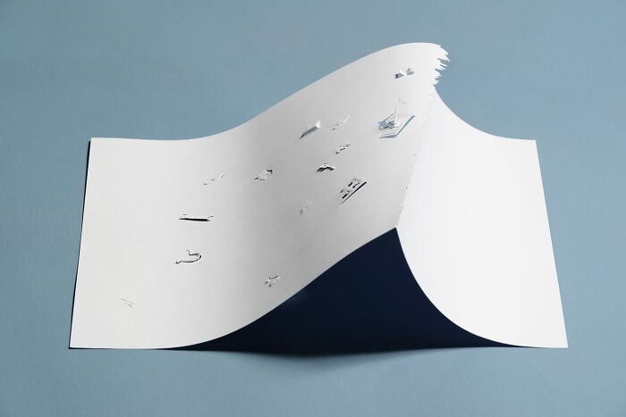 Paper art by Peter Callesen featuring a detailed mini world on a curved white sheet.