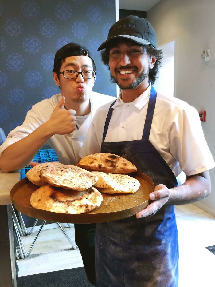 Dos panaderos sonrientes mostrando pan recién horneado, un momento positivo para recobrar la fe en la humanidad.
