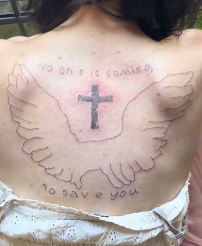 Back tattoo with a cross and wings surrounded by handwritten text, showcasing a wild tattoo fail on skin.