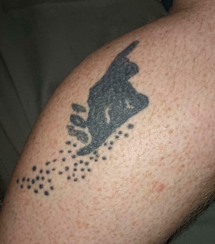 Close-up of a wild tattoo fail on a person's arm showing a poorly designed black silhouette with scattered dots.