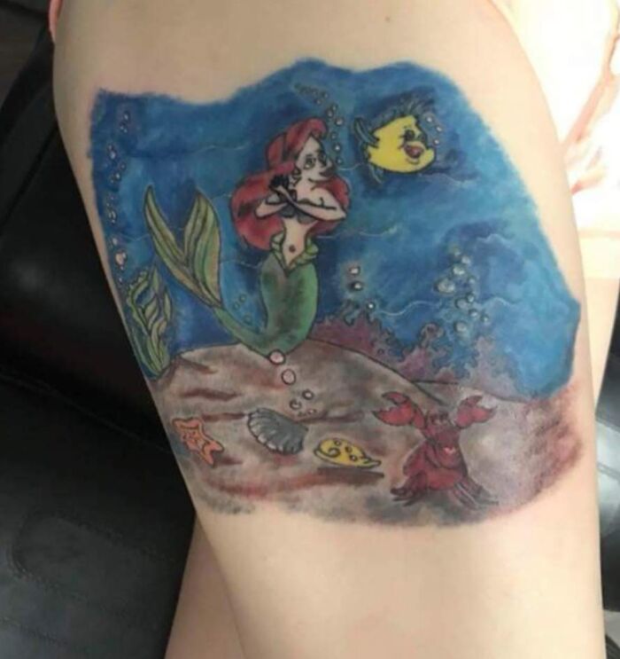 Tattoo fail of a mermaid and sea creatures with distorted and unclear design on a person's upper arm.