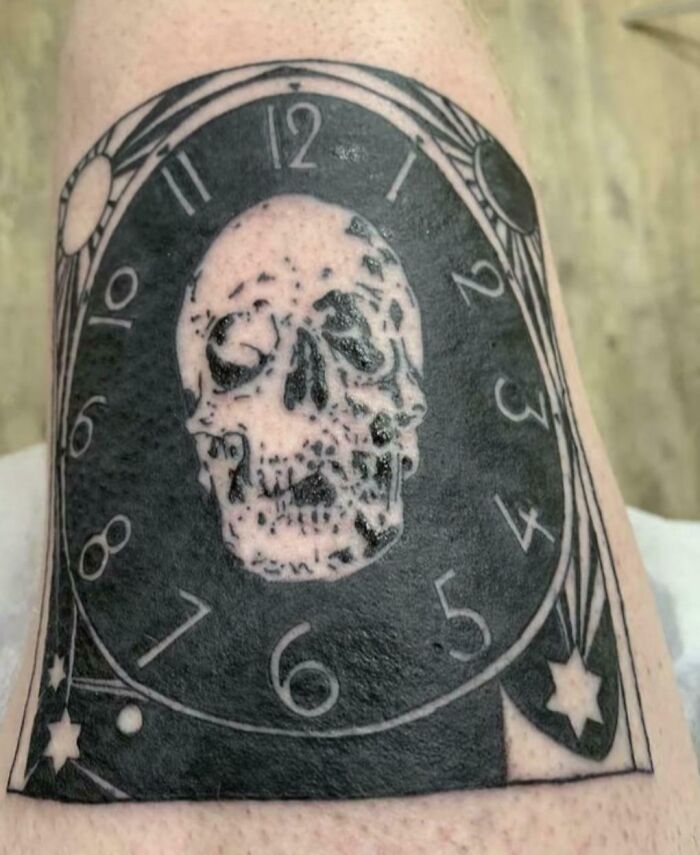 Tattoo fail of a clock with distorted numbers and a skull in the center, showcasing a wild tattoo mistake on skin.