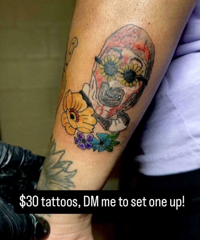 Brightly colored tattoo fail featuring a distorted skull with flower eyes and additional floral designs on forearm.