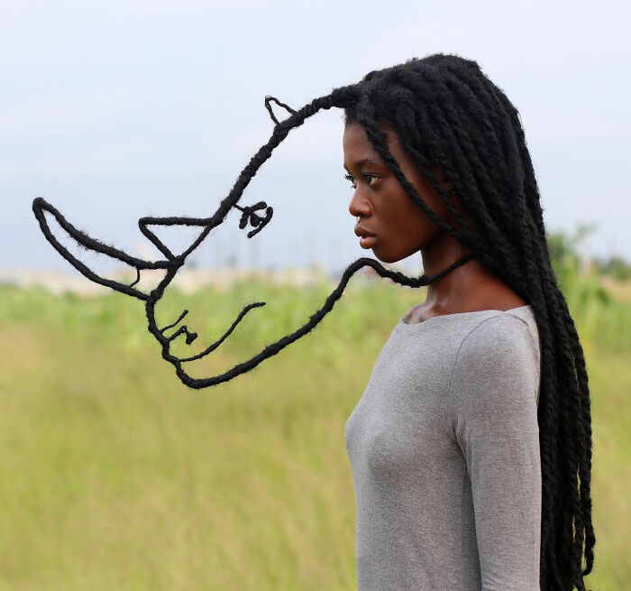 Artist's hair sculpture resembling a face, with intricate design, set against a natural outdoor background.