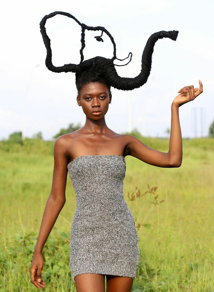 Woman with hair sculpture resembling an elephant in a field, showcasing artistic hair transformations.
