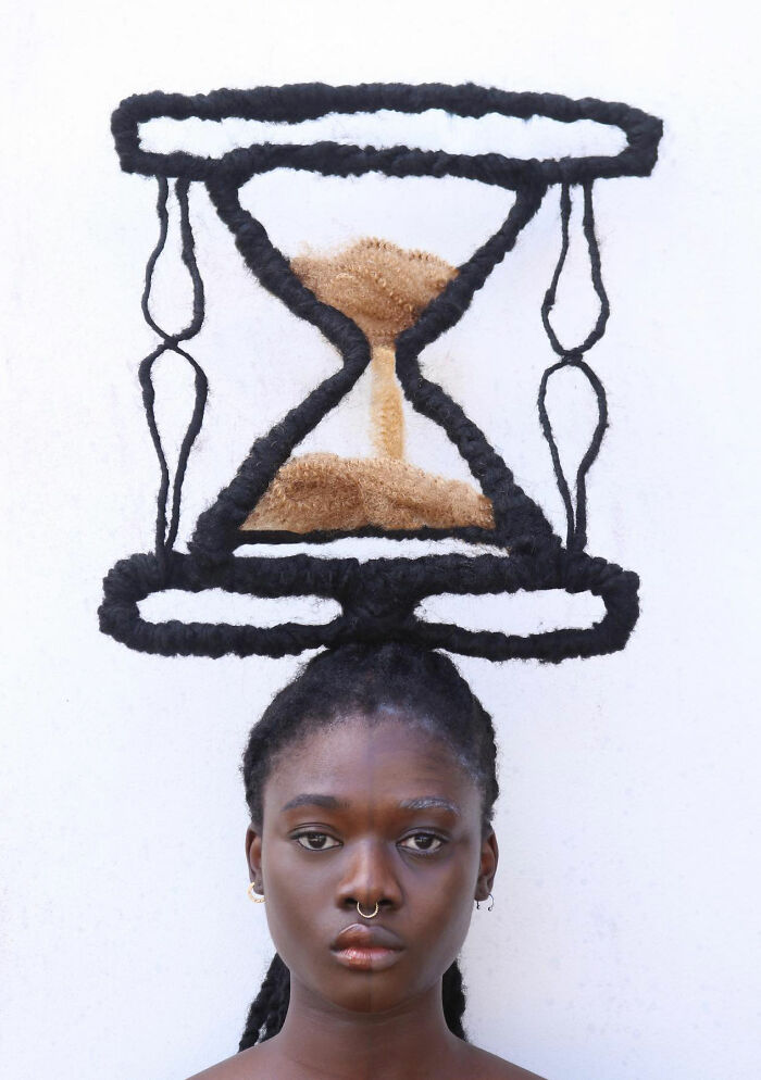 An artist with hair sculpted into an intricate hourglass design against a white background.