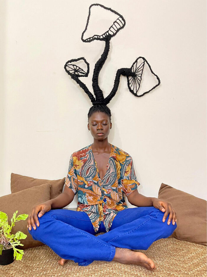 Woman with hair sculpted into artful mushroom shapes, sitting cross-legged.