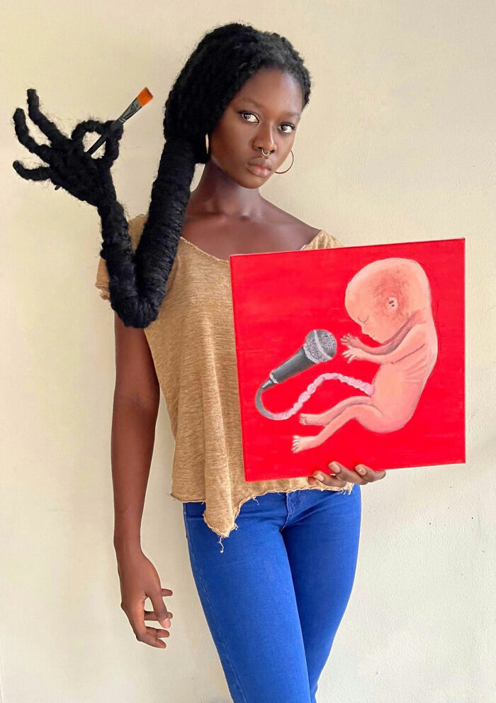Artist with hair sculpture holding a painting, showcasing intricate creative expression.