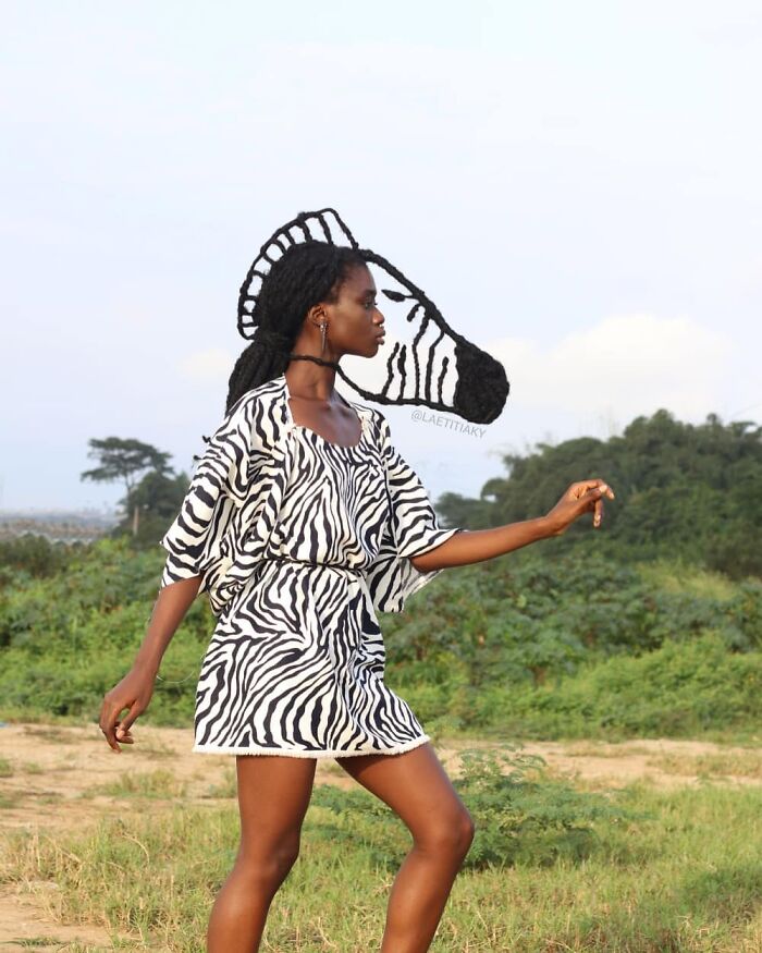 Artist with zebra hair sculpture, wearing zebra-pattern dress, walking outdoors.