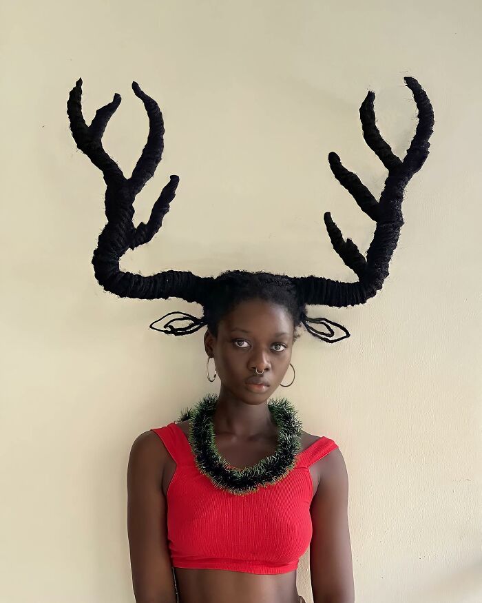 Woman with hair sculpture resembling antlers, wearing a red top and hoop earrings, showcasing innovative hair art.