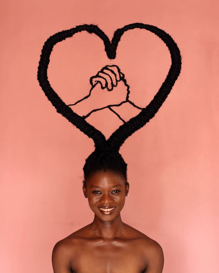 Woman with a stunning hair sculpture shaped into a heart and clasped hands on a peach background, showcasing incredible hair art.