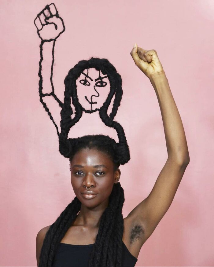 Artist with hair sculpture of a raised fist, set against a pink background, celebrating creativity and expression.