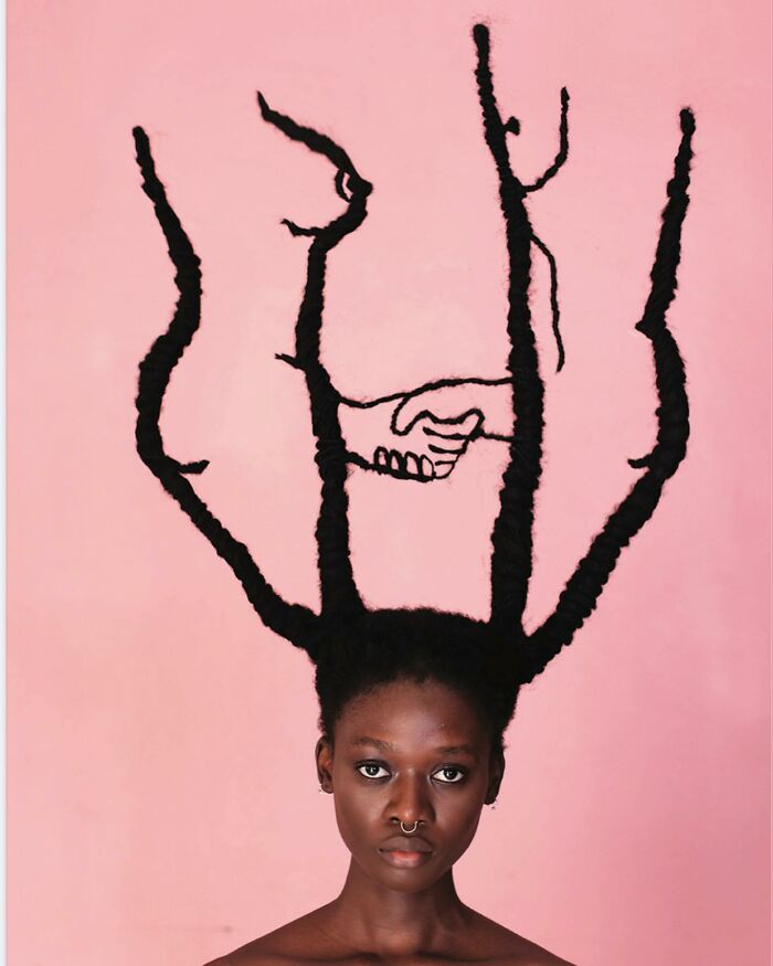 Woman's hair styled into intricate sculpture against pink background.