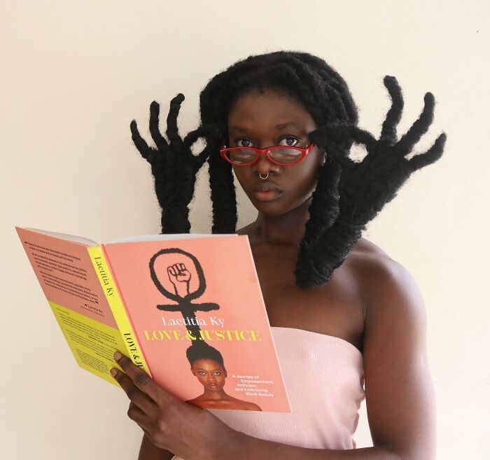 Woman reading a book with unique hair sculptures, wearing red glasses.