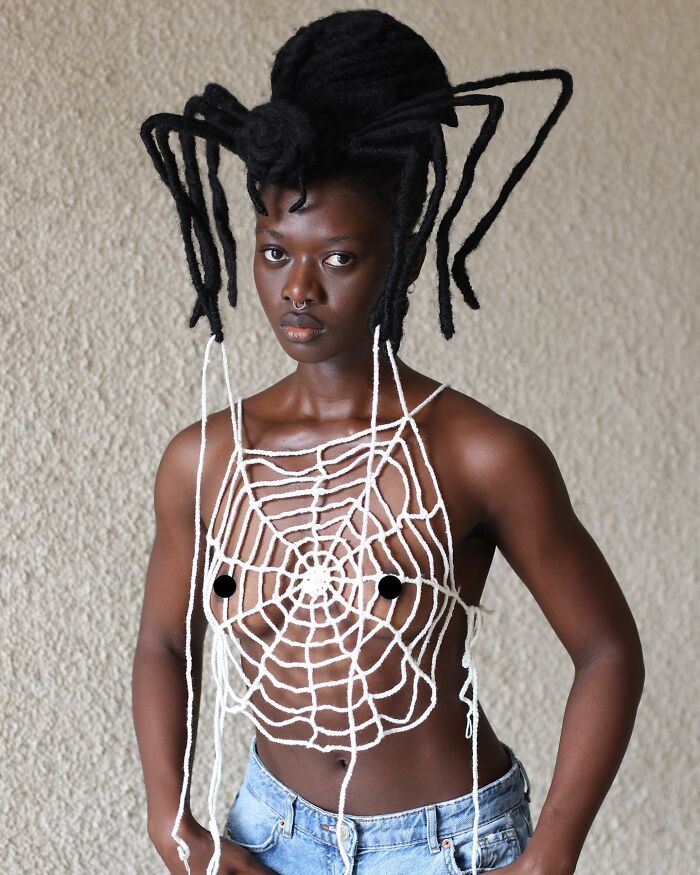 Artist's hair sculpted into spider shape, wearing web-like top and jeans.