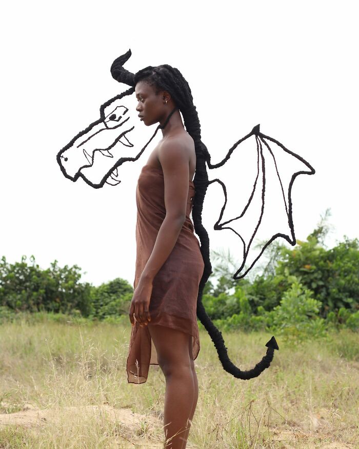 Artist with intricate hair sculpture resembling a dragon in a grassy landscape.