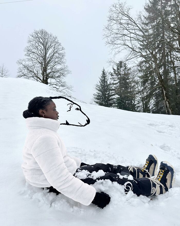 Woman seated in snow, her hair creatively sculpted to resemble a polar bear, with trees in the background.