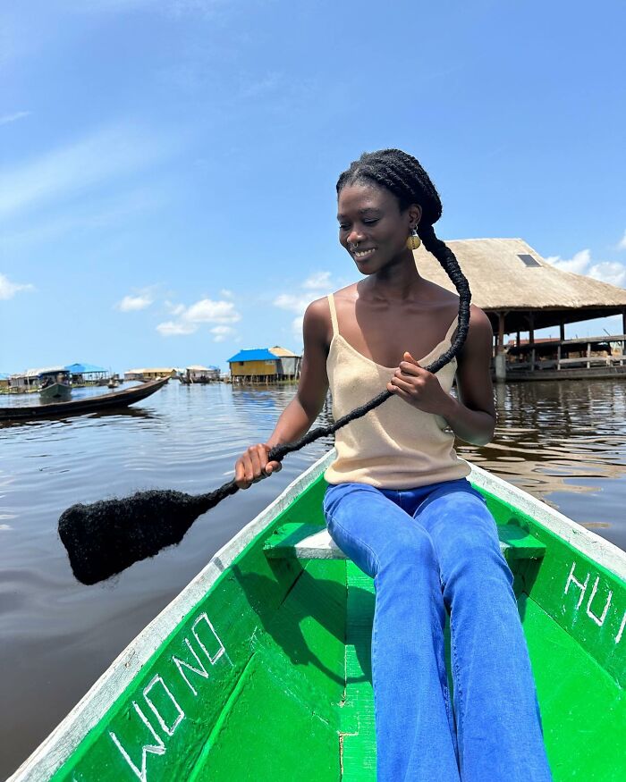 Woman in a boat, using her hair as a paddle, showcasing incredible hair sculpture artistry.